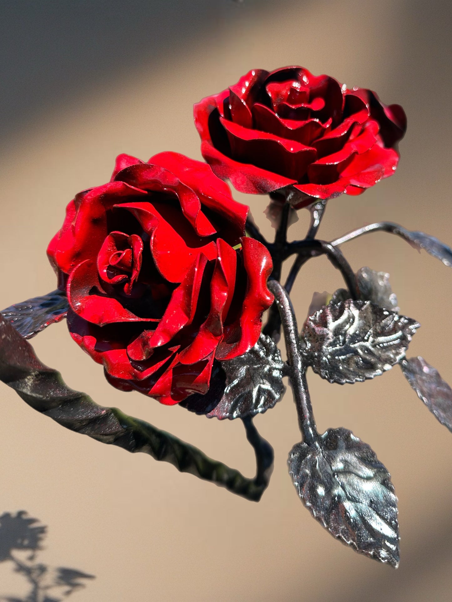 “Hand-forged steel heart frame hanging against a softly lit background, featuring red metal roses and textured steel leaves arranged at the centre.