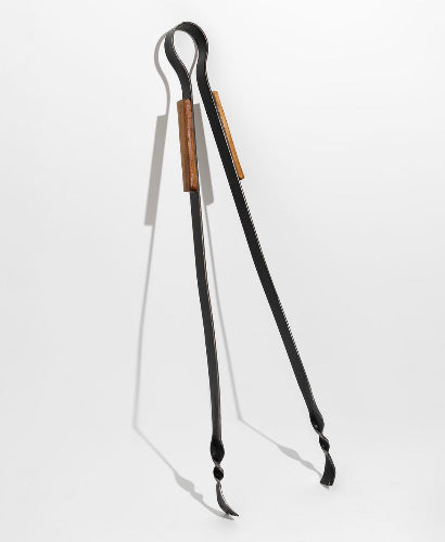 These are steel tongs which have been hand forged by the blacksmith at all fired up, they are steel and wood and are leaning on a white wall with dramatic shadows because they know they are stunning